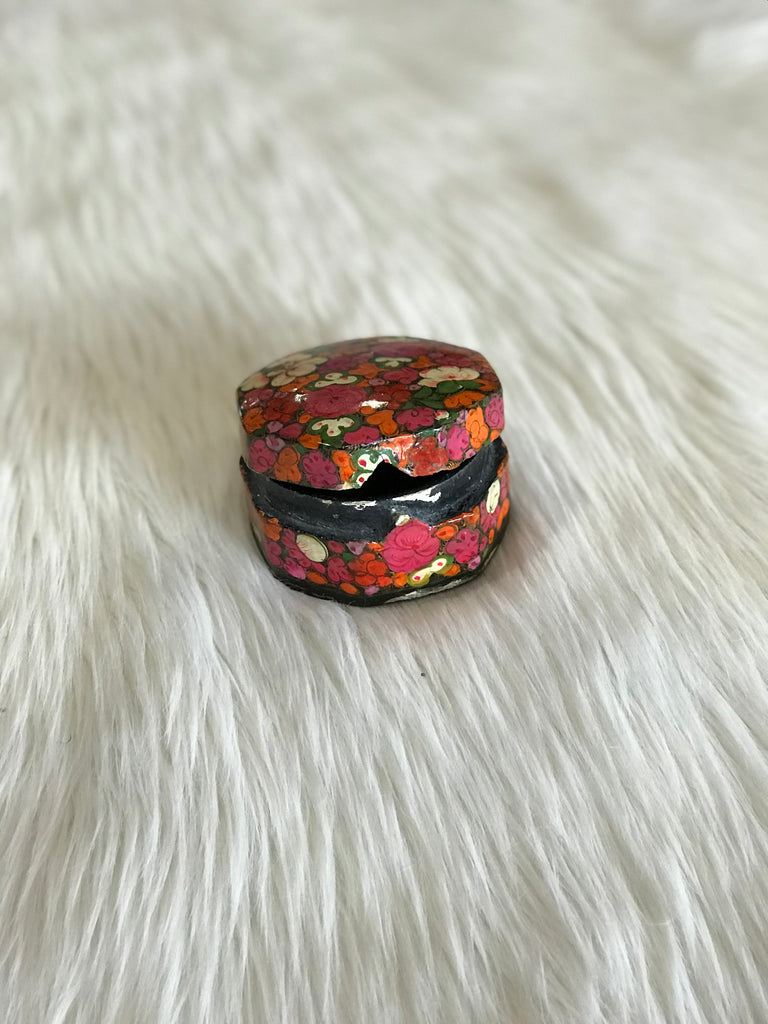 A vintage, rounded-octagonal, lidded box with hand-painted bright pink, orange, and white floral design and a black, lacquered interior. Triangle-shaped notch closure shown here